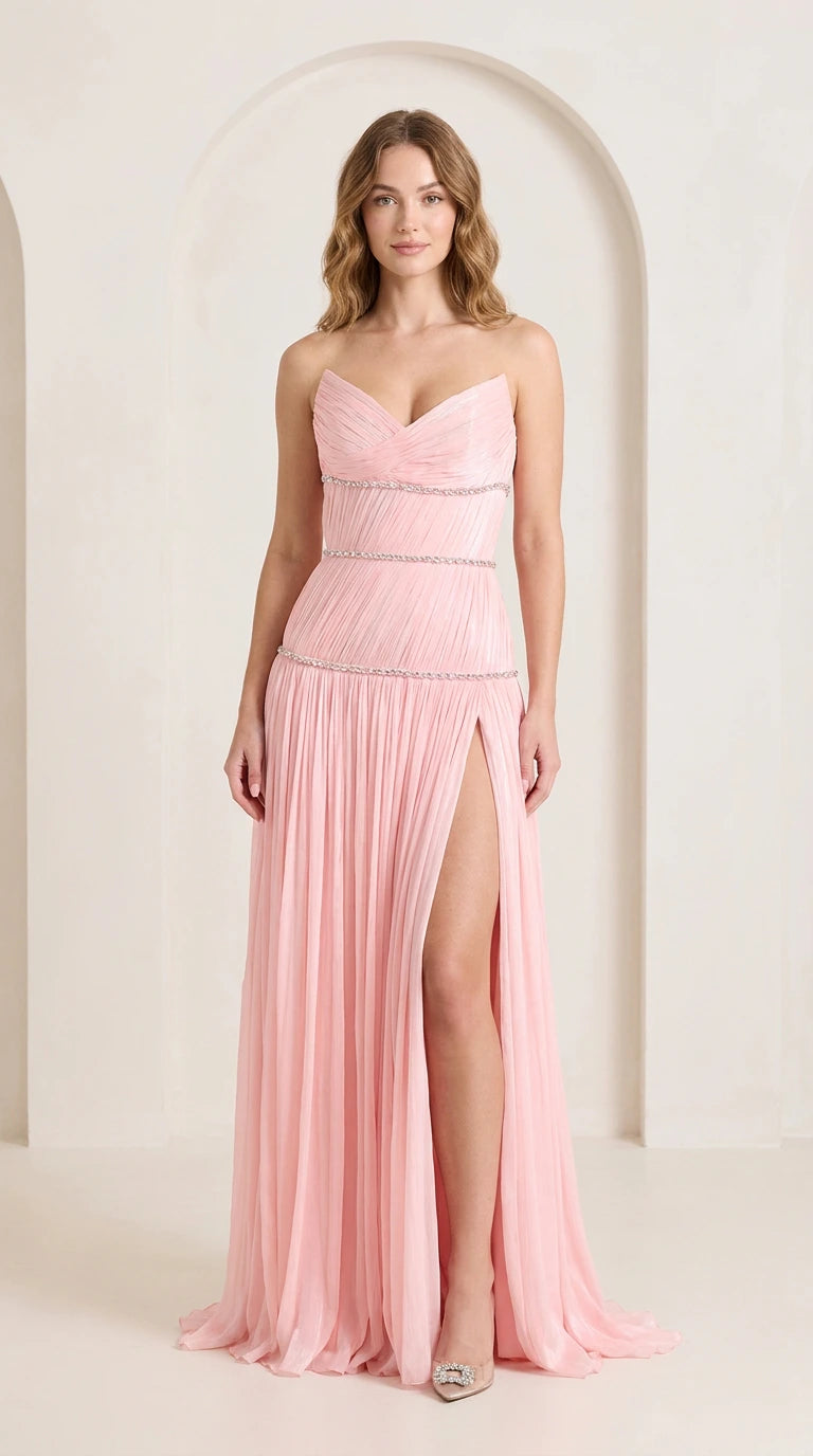 Front view of woman wearing strapless blush pink pleated evening gown with rhinestone trim and high slit