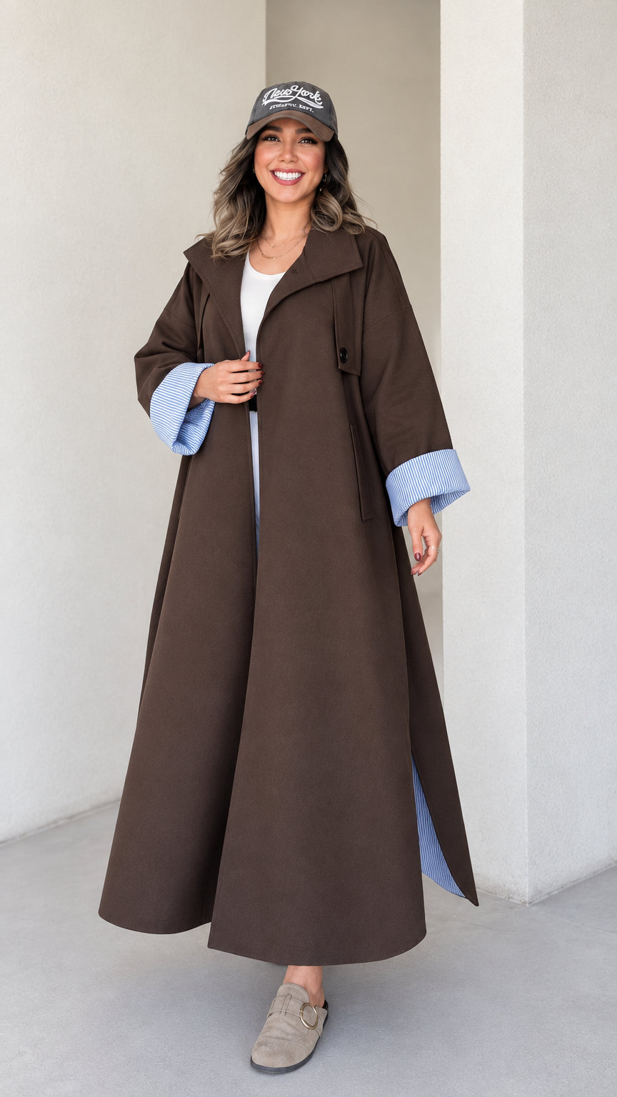 Front full view of woman wearing brown maxi trench coat with striped turn-up cuffs