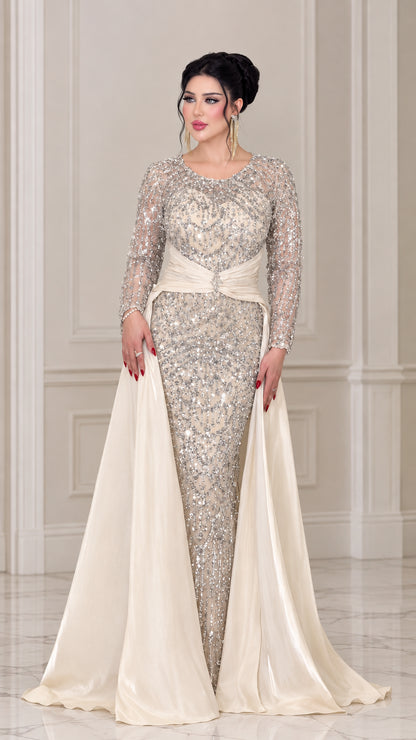Front view of woman wearing a champagne sequin long sleeve evening gown with satin overskirt