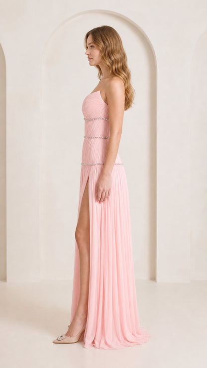 Side profile of woman in strapless blush pink pleated maxi gown showing thigh-high leg slit