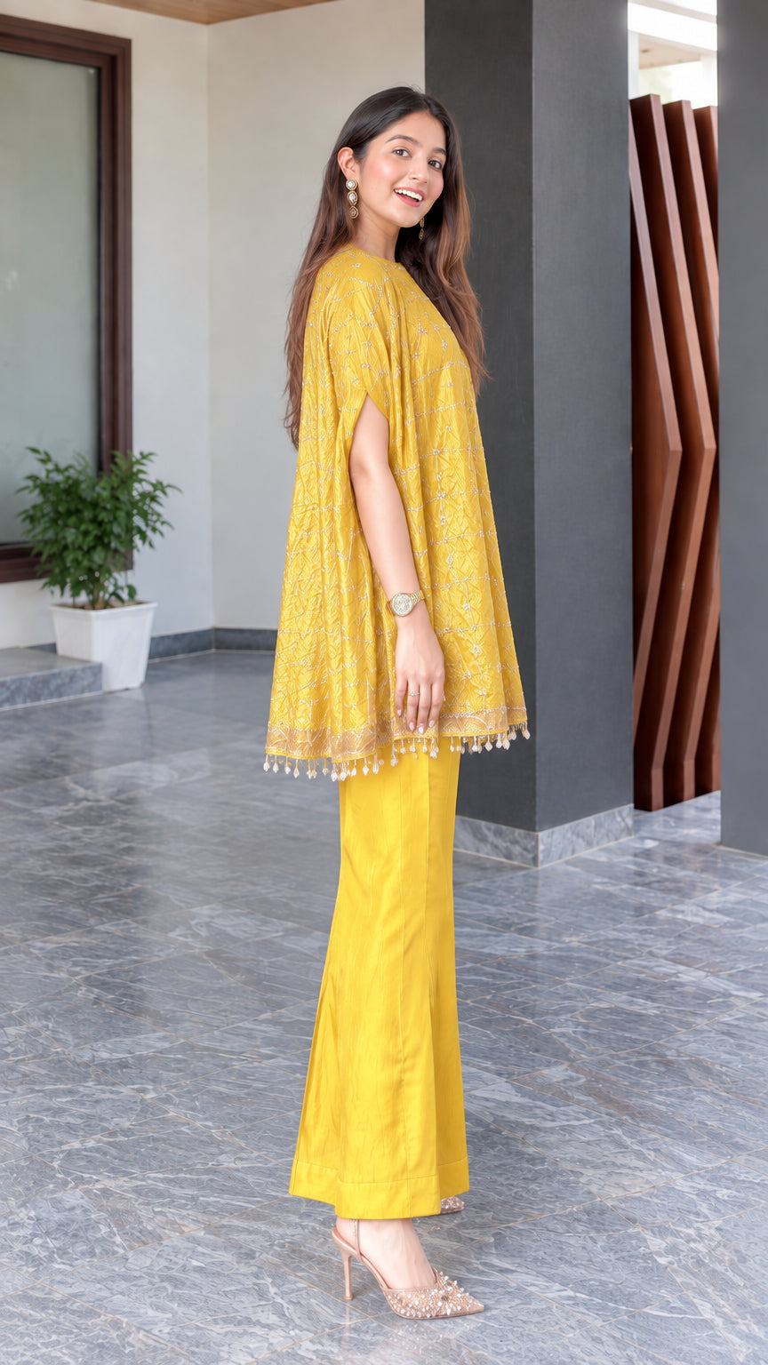 Side angle view of model in mustard yellow embroidered cape top and matching wide-leg trousers