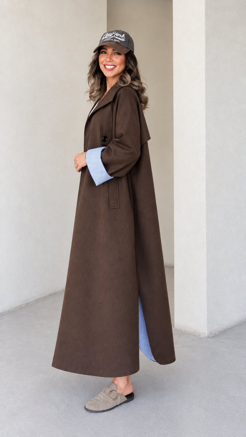 Side profile view of brown flowing maxi trench coat showing striped side slit detail
