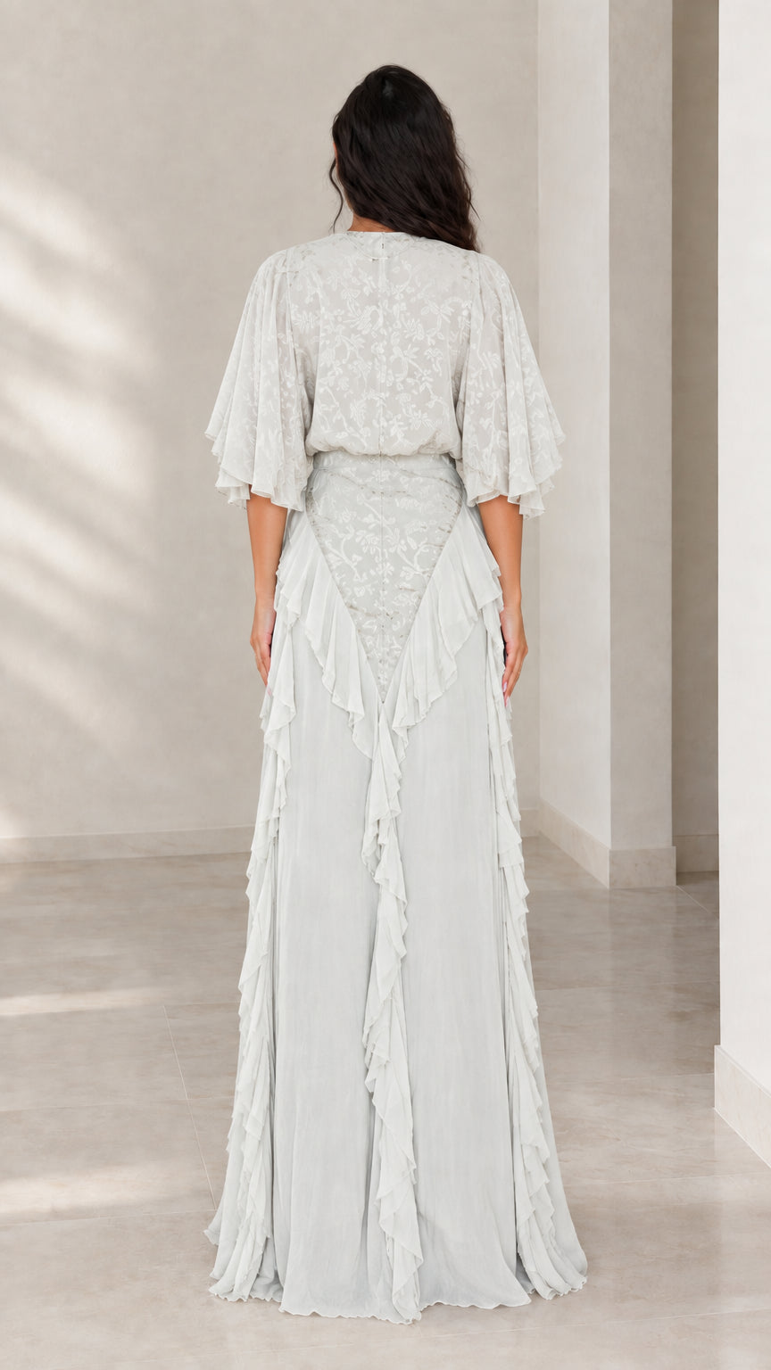 Back view of woman wearing ice blue flutter sleeve maxi gown with ruffle details