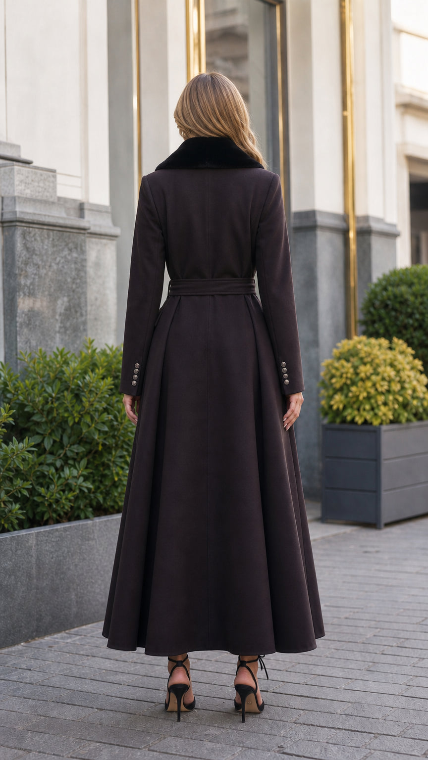 Back view of model in dark brown belted long coat showcasing pleated maxi hem