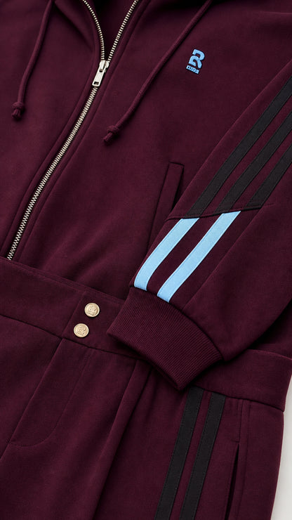 Close-up detail of burgundy zip-up jacket cuff, sleeve stripes, and waistband buttons
