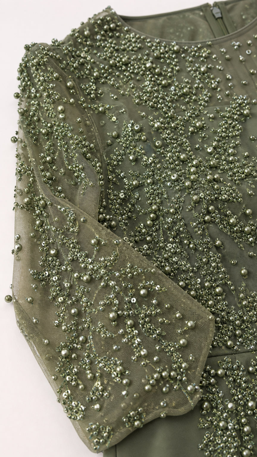 Close-up detail of ornate beadwork and pearl embellishments on green lace sleeve
