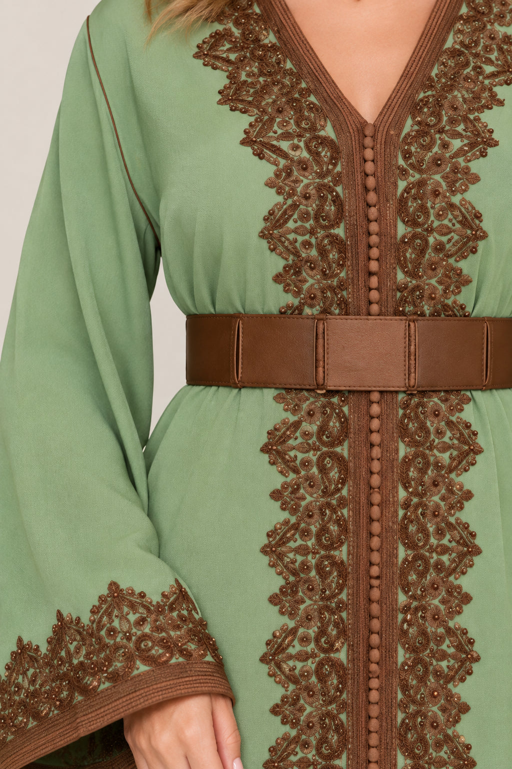 Close-up of brown lace embroidery and belted waist on green dress