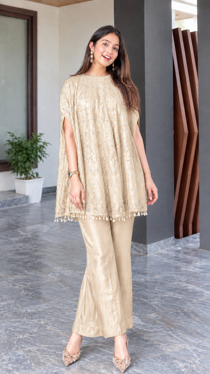 Model wearing champagne beige embroidered cape tunic and matching flared trousers